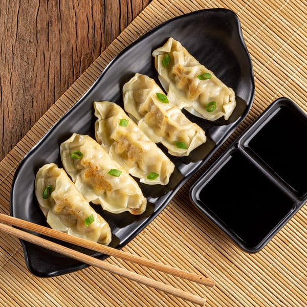 Five golden-brown Lucky Chopsticks dumplings with green onions on a black plate with soy sauce and chopsticks.
