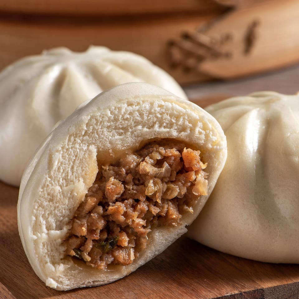 Steamed Chinese bun (baozi) with a savory meat filling, cut open to show the inside.