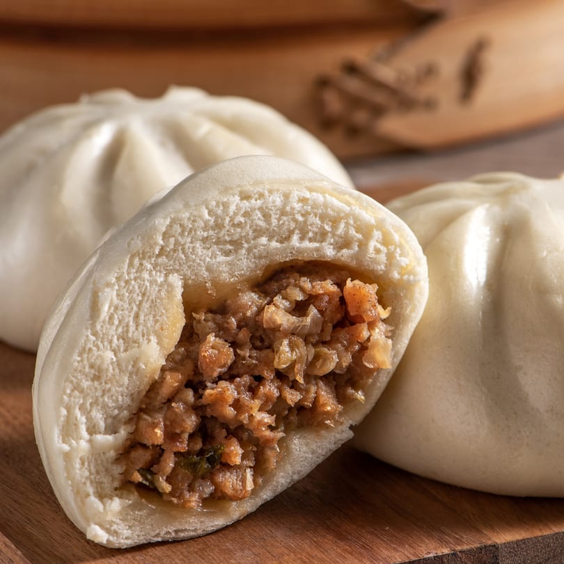 Steamed Chinese bun (baozi) with a savory meat filling, cut open to show the inside.
