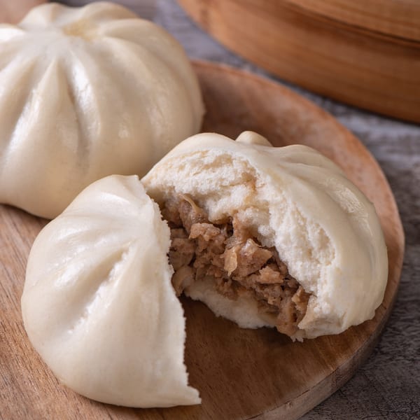 Two Lucky Chopsticks steamed buns on a wooden board, one split open revealing savory meat filling.